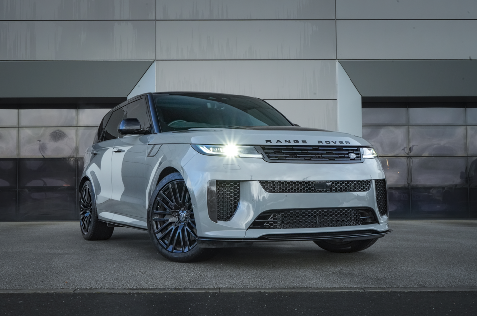 Silver Range Rover with headlights on, parked on a concrete surface.