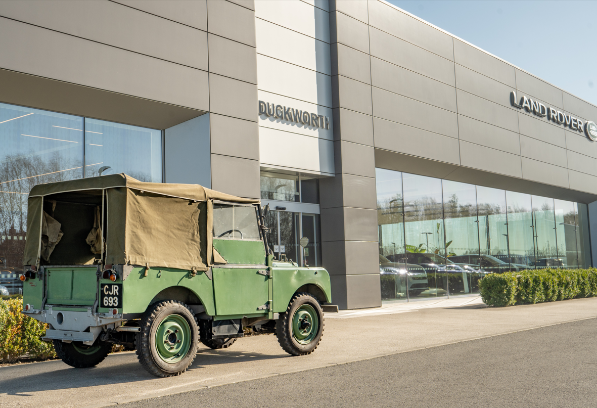 Green vintage Land Rover parked outside a dealership.
