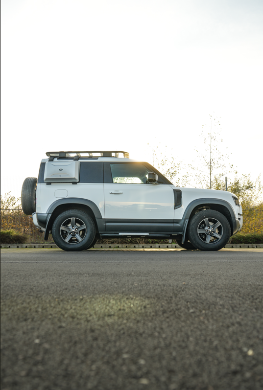 Side view of a silver off-road vehicle with a roof rack and spare tyre.